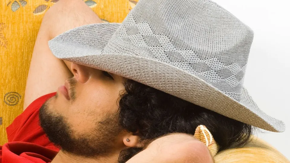Uomo con barba e cappello che riposa su un divano giallo